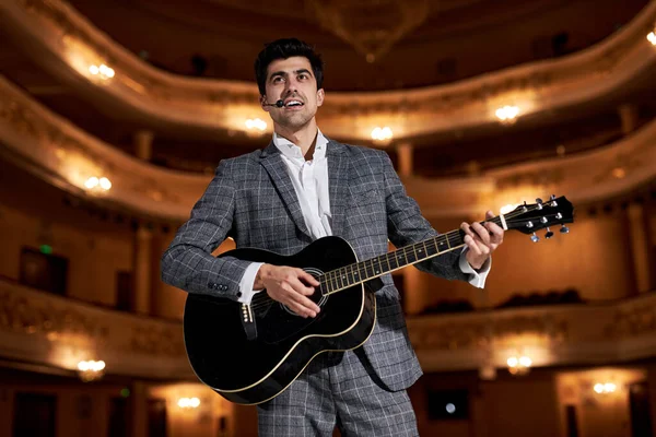 singer Guitar player in elegant classic suit performing playing guitar solo sound at concert standing on stage. handsome caucasian guy performing music for audience. art, music concept