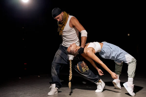 Black and caucasian couple dancing contemporary dance in studio.black background. Dance lessons. Hip Hop dance performance on stage. Man, woman giving performance together, dancing in hip hop style
