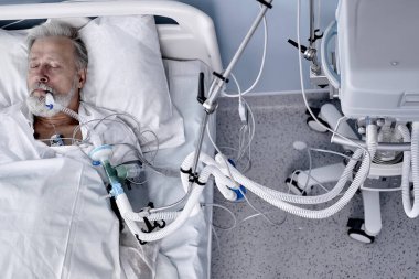 sick caucasian senior patient lies on bed in modern hospital , Saline intravenous drip on hand. coronavirus, covid-19, medicine, health concept. Virus and illness protection. top view