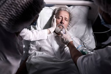 unrecognizable doctors nurses save a patient from death lying on bed in hospital, the patients heart rate slows down, at night time. elderly man suffering from disease, heart attack, pneumonia