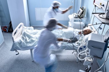 unrecognizable doctors nurses save a patient from death lying on bed in hospital, the patients heart rate slows down, at day time. senior man suffering from disease, heart attack, pneumonia