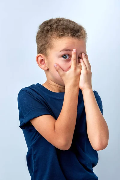 emotional little boy covers face with hand isolated over pink background, frightened child watching horror film, movie, reaction, facial expression. human children emotions concept