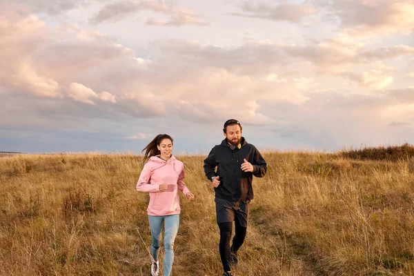 Young Couple Running On Field In Morning. Caucasian Man And Woman On Jogging Workout, In Sports Clothes. Male And Female Exercising, Training Together, Lead Healthy Lifestyle. Fitness Concept