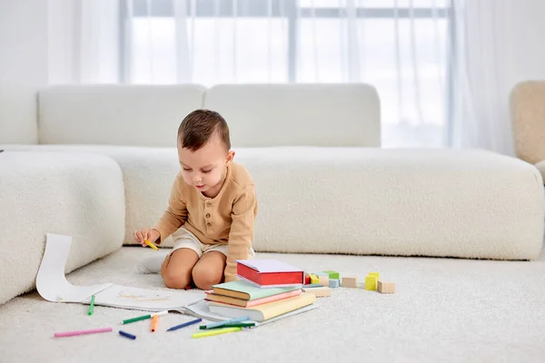 cute little boy draws on warm floor in bright living room. happy caucasian child draws with pencils. Childrens leisure. Family and children concept. lovely boy in casual clothes, alone.