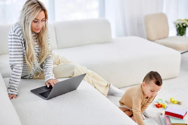 Young Blonde Caucasian Female Mother Sitting Sofa Working Laptop While — Stock Photo, Image