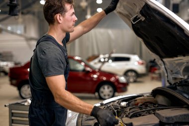 professional Auto mechanic working under car hood in repair garage, closing or opening the hood, working alone. car service, repair, maintenance and people concept. at modern clean workshop