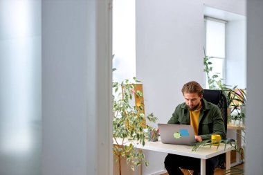 american man working with modern laptop in office, young manager working online, typing emails or chatting with clients. handsome european guy with beard dressed casually. business, sales, profession
