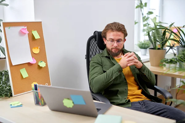 bearded male working alone in modern office, using laptop. handsome guy sit thinking, being proficient. successful office worker. caucasian european guy in casual wear concentrated on thoughts