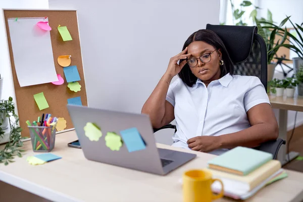 remote job, technology and people concept. tired young black woman with laptop computer working, want to go home, overthinking, exhausted by work in office. alone. black female having headache