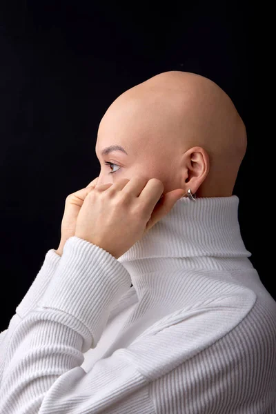 Bald female posing for images supporting Cancer Awareness or alopecia problem campaigns worldwide. isolated black studio background. side view portrait of hairless lady covering face with white shirt