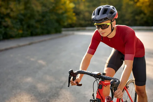 快一点严肃的年轻高加索男子赛车手穿着运动服 戴着防护头盔 骑自行车时看起来很专注 在大自然的乡村和大自然中骑车 夏季体育活动 — 图库照片