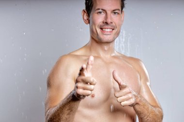 Happy shirtless young man with perfect skin showing at you, look at camera, having sexy muscular body, isolated on gray studio background, portrait. Skin care healthcare cosmetic procedures concept