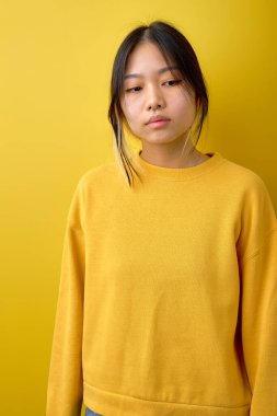 sad melancholic female of asian appearance posing looking down thinking, isolated over yellow background, dressed casually. upset woman having deep thoughts, need rest, tired exhausted