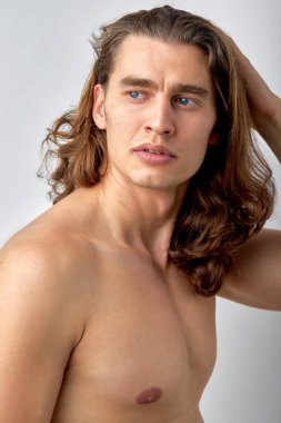 confident male model is touching long hair, head, enjoy having healthy face skin, look at side posing at camera, isolated over white studio background. portrait. people, lifestyle, beauty
