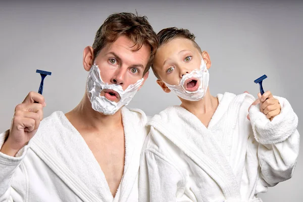 caucasian male and little boy having fun with shaving foam on faces in bathroom, isolated. Funny Happy Father and son shaving faces in the morning together, making crazy faces, weekends