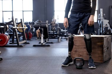 Modern spor salonunda ağırlık antrenmanına hazırlanan sakat ve protez bacaklı bir adamın kesilmiş görüntüsü. kopyalama alanı, bulanık arkaplan. güçlü sağlık hizmetleri