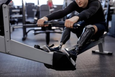 Engelli kişi spor merkezinde kürek çekme makinesi kullanır, kırpılmış atış, yapay bacak yaşam tarzı sağlık ve vücut bakımına odaklanır