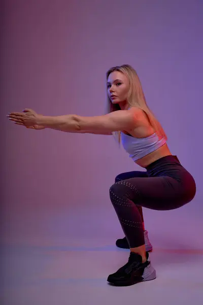 fair-haired slim well-built woman performing squats with raised arms forward, full length side view shot. coordination, balance