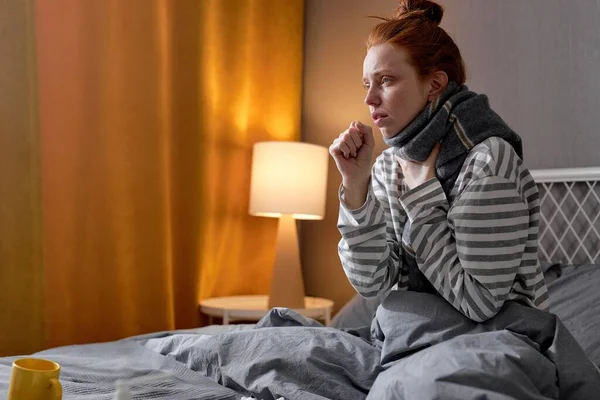 young ginger woman coughing touching neck and feeling pain in throat sickness, have fever, flu ill on bed, couch at home. Health, cold seasonal influenza person and virus concept. closeup portrait