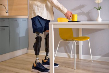 Biyonik zeka protezinin üzerinde duran engelli ya da engelli bir adam evde kahve ya da çay yapıyor. Kapalı alanda. Evde kal. Sabahleyin. engelli yaşam tarzı