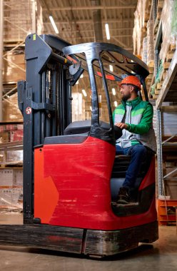 Depodaki koruyucu güvenlik üniformalı adam forklift yükleyicisiyle çalışıyor. Fabrika deposunda profesyonel forklift şoförünün portresi. lojistik, ulaşım endüstrisi