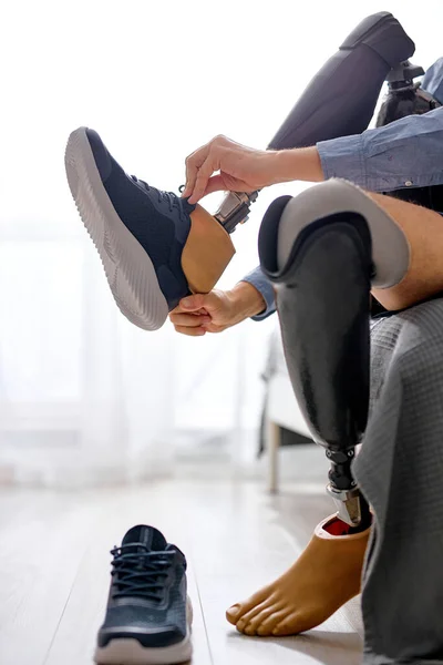 ベッドに座っている自宅の義足にスニーカーを着用した 認識できない手術を受けた男の足のアンプティーは 事故後の障害を負った その日のために準備している男 — ストック写真
