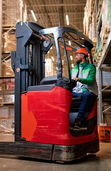 man in protective safety jumpsuit uniform in hardhat at warehouse works with forklift loader. Portrait of professional forklift driver in factorys warehouse. logistics, transportation industrial