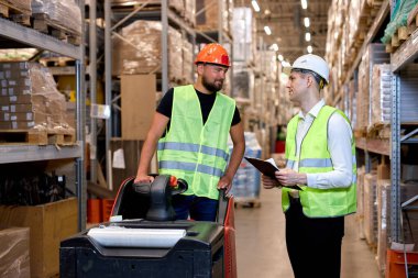 Kafkasyalı genç işçiler depodaki raflarda stok yapıyorlar, pano ve forklift kullanıyorlar, tartışıyorlar, kontrol ediyorlar ve kontrol ediyorlar. Envanter sayımı kavramı