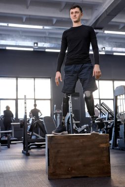 Spor giyimli hırslı bir adam kutunun üzerinde duruyor, uzun bir fotoğraf. Boş zaman, boş zaman, sağlık ve vücut bakımı. İyilik