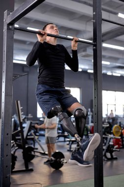 Modern spor salonunun barında barfiks çeken protez bacaklı hırslı bir adam. Tam boy yan görüş, boş zaman, boş zaman, yaşam tarzı.