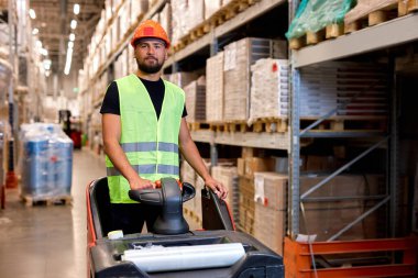 Forklift sürücüsü depoda. Yük taşımacılığı, Depo endüstriyel teslimat, genç beyaz erkek nakliye ekipmanları, yeşil üniformalı yelek ve güvenlik kaskı giymiş.