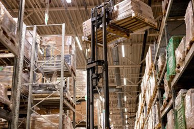 Forklift kargo kutularını kargo lojistiği, ulaşım endüstrisi ve teslimat konseptinde depolama deposundaki raflara koyuyor.