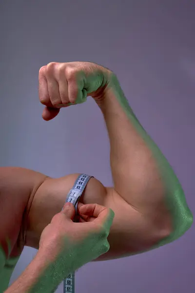隔離された青い背景を測定するテープが付いている強い筋肉の男性の手のクロップされたショットを閉めて下さい ロイヤリティフリーのストック写真