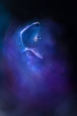 Genç bir bayan dansçı, kollarında parlak peçeleri olan çiçek yapraklarını taklit ediyor..