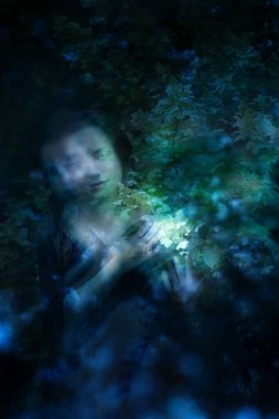 Çifte yansıtma etkisi olan bir kadın karanlıkta parlayan bir Hortensiya çiçeği tutuyor..