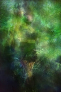 Yumuşak, bulanık dansçı, canlı yeşil ışık dokularıyla bir peçenin altında zarifçe poz veriyor..