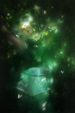 Siyah kelebek dantelli rüya gibi bir kadın, arka plandaki yaprakların arasından parlayan, güneş ışığıyla kaplı, pohpohlayan kelebeklerle çevrilidir..