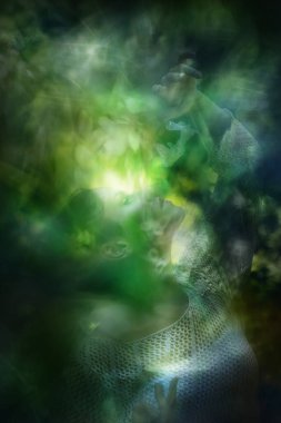 Örülmüş bluzlu bir kadın, parlayan yeşil bir arka planın önünde, elleri arasında süzülen dekoratif dantel kelebekleri izliyor..