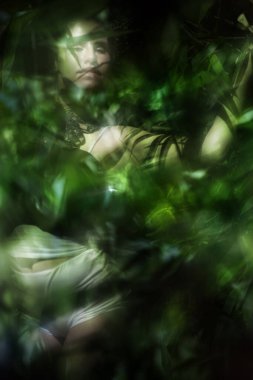 Beyaz külot ve siyah kelebek danteli giymiş ritmik bir şekilde poz veren genç bir kadının bulanık tropik sahnesi..