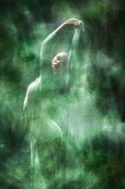 Çekici bir kadın sanatçı, etrafında katmanlı şelale dokuları olan beyaz bir peçe tutuyor. Beyaz boho elbisesi, örülmüş bir yaprak dokusuna sahip, çevresindeki tropikal yapraklara benzer..