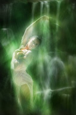 Genç, zarif bir kadın, büyük bir tropikal yaprağı anımsatan beyaz örgü bir kostüm içinde poz verirken, uzun şelale dokularına geçiş yapan şeffaf bir peçe tutuyor..