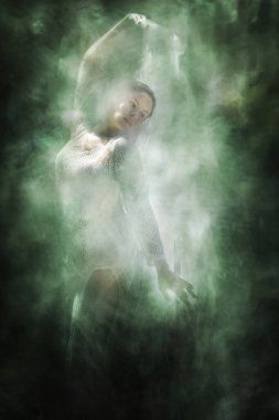 Şelale dokusuna gömülü şeffaf bir peçe tutan, örülmüş yaz elbisesi giymiş genç bir kadın dansçı..