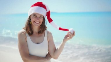 Kumsalda uzun dalgalı saçları ve çizgili Noel şapkası olan beyaz mayolu zarif bir kadın..