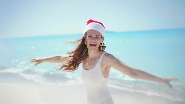 수영복을 머리에 줄무늬 크리스마스 모자를 여성이 웃으며 해변에서 즐거운 시간을 — 비디오