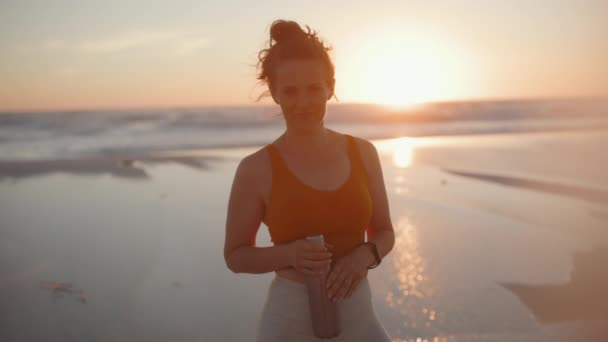 フィットネスの女性のジョガーは夜にビーチで水のボトルとフィットネス服を着て — ストック動画