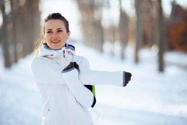 Beyaz ceketli mutlu kadın kışın şehir parkında geriniyor..