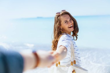 Sahilde beyaz çizgili tişört ve şortla eğlenen 40 yaşında bir kadın..