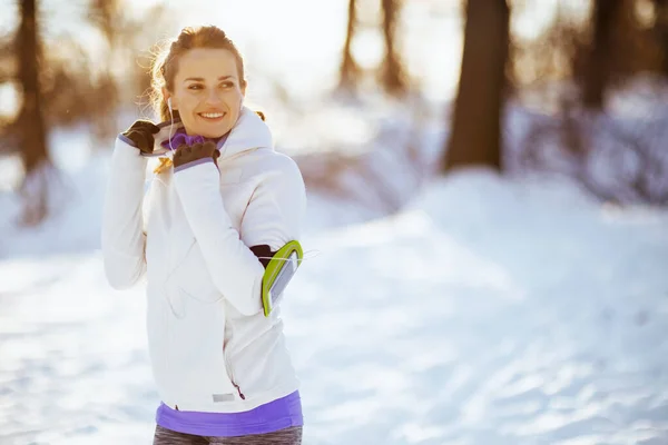 stock image smiling fit woman in white jacket with headphones outdoors in the city park in winter.