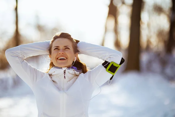 stock image happy active woman in white jacket with headphones outside in the city park in winter.