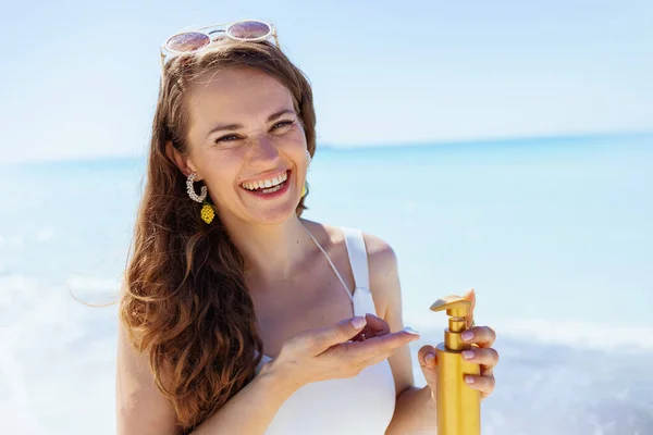 Stock image Portrait of happy stylish female at the beach in white beachwear using spf.